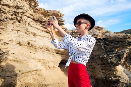 Beautiful woman with mobile phone on background of rock near seaの写真素材