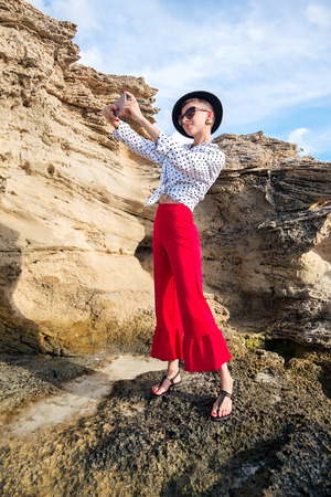 Beautiful woman with mobile phone on background of rock near seaの写真素材