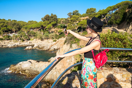Woman taking pictures of beautiful seashore with rocks and vegetationの写真素材
