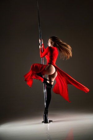 Slim woman in a sexy red dress and black stocking dancing on a pylonの写真素材