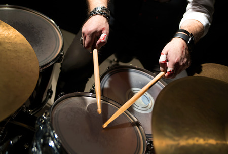 Drummer with a drumsticks in his hands playing on drum set on stage on the black background