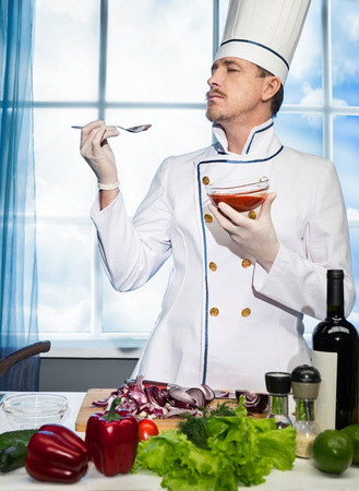 Cook in white uniform stands tests the sauce from the spoon in the kitchenの写真素材