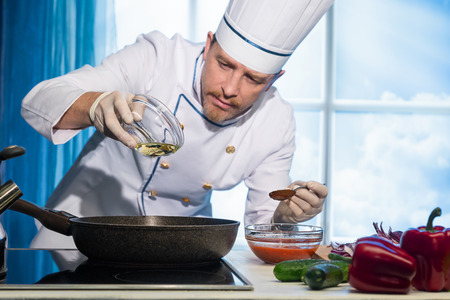 Cook in white uniform pours vegetable oil into the pan in the kitchenの写真素材