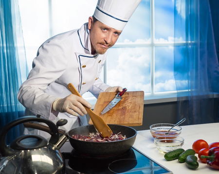 Cook in white uniform puts sliced onions in the panの写真素材