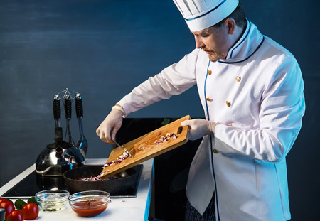 Cook in white uniform puts sliced onions in the panの写真素材