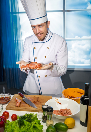 Cook in white uniform holds in his hands a piece of chicken in the spicesの写真素材