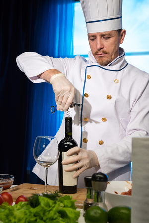 Chef in white uniform opens a bottle of wineの写真素材