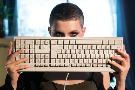 Young female hacker covers her face with a keyboardの写真素材