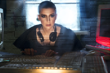 Female hacker at the computer over code backgroundの写真素材