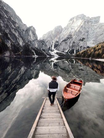 A man goes down the stairs to a wooden boat against the reflection of mountains in the water