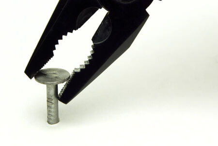 nail on a white background and black pliersの写真素材