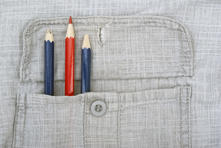 One sharp red pencil and two blunt pencils in a pocket of a gray shirtの写真素材