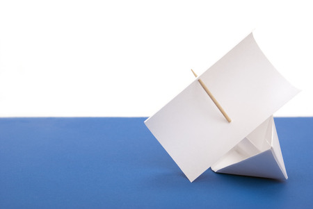 Paper ship with a sail on a white and blue surface
