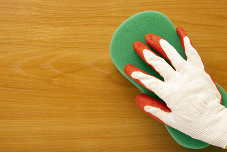 Hand in it is white to a red glove and a green sponge against the background of a brown board
