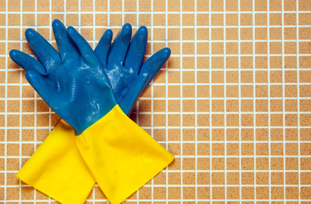 Two blue with yellow color rubber gloves on the background of brown cells, tiles.の写真素材