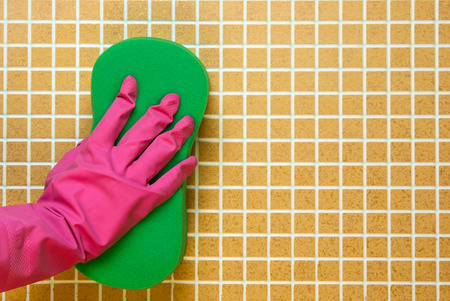 Hand in glove with pink sponge green on brown wall in the cellの写真素材