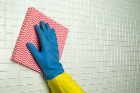 pink rag to clean with a hand in blue with yellow glove on the white cellsの写真素材