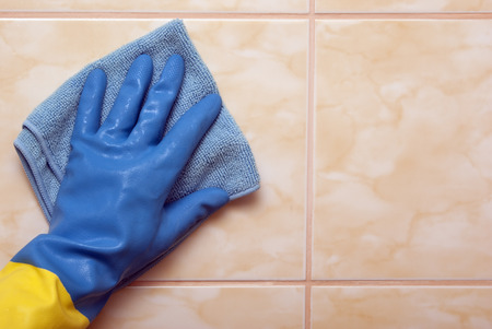 Hand in blue with yellow glove with blue cloth on the wall tilesの写真素材
