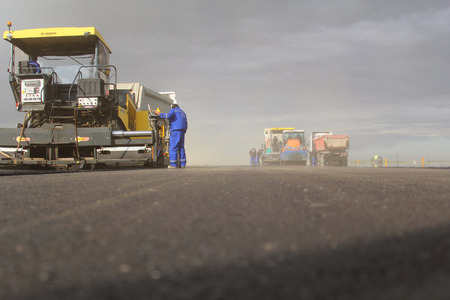 TULCEA, ROMANIA - NOVEMBER 08: Tracked paver laying fresh asphalt pavement on a runway as part of...