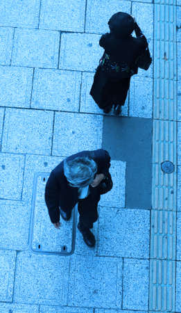 A man and a woman walking in different directions on a city street-upper blue viewの写真素材