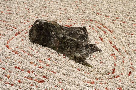 Detail of a Japanese garden with sand,rock and few maple leaves.