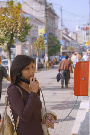 Image of a young woman at the public phone in a city street.の写真素材