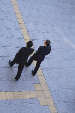 Two businessmen walking in a city.Slighty motion blur on the pavement and on the left person,main focus on the right man.の写真素材