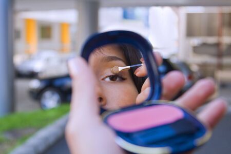Close-up of a young woman eye looking in a mirror in a city street.の写真素材
