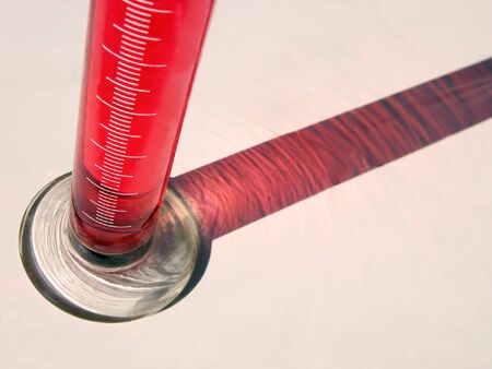 Tube with a red substance and its shadows on the desk...chemical lab abstract..focus on the base of the tube          の写真素材