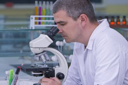 Male researcher looking through a microscope in a laboratory.