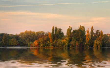 Beautiful forest reflected in the lake in a fall sunset.Location:Herastrau Lake,Bucharest,Romania.の写真素材