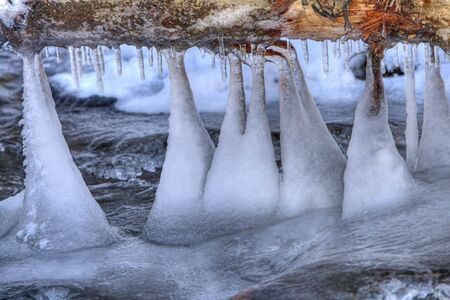 Ice formation on a frozen river under an overturned tree trunkの写真素材