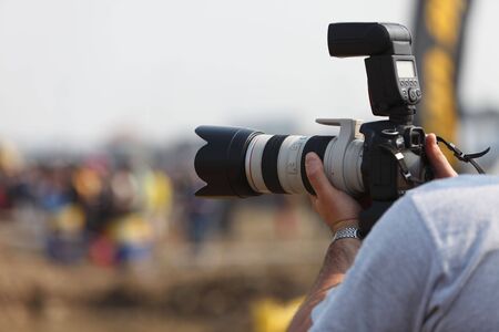 Detail of a photographer's hands holding a DSRL camera with a long zoom high end lense attached.