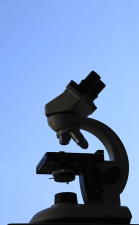 Black silhouette of a microscope against a blue sky.