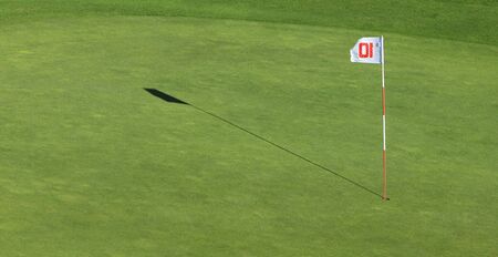 A flagpole and its shadow near the hole on a green golf field.の写真素材