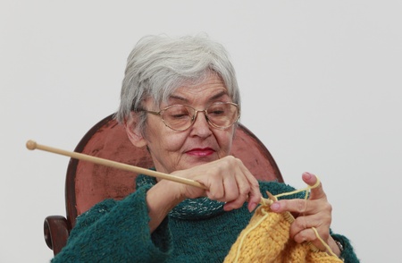 Portrait of an old woman knitting,against a gray background.