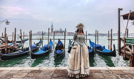 Venice, Italy- February 198th, 2012:A woman ina beautiful dress and colombina mask posing in front of gondolas dock during the Venice Carnival.のeditorial素材