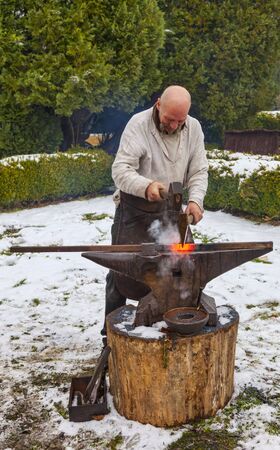 Rodemack,France- December 09, 2012:Aedieval blacksmith hammering a piece of hot red fire outside in winter during a reenactment historical festival in Rodemack in France.のeditorial素材