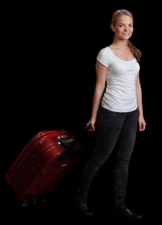 Young blonde woman with a red suitcase walking against a black background.の写真素材