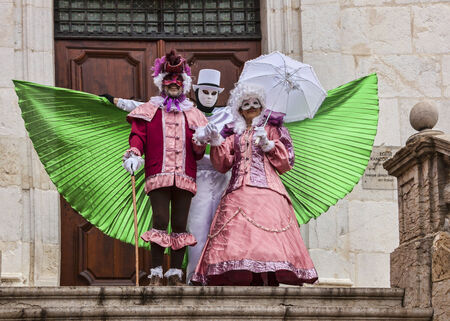 Annecy,France-March 15,2014 Three disguised persons show a beautiful scene in front of a wooden gate during the Annecy Venetian Carnival  Yearly in Annecy ,France is held a Venetian Carnival to celebrate the beauty of the real Venice のeditorial素材