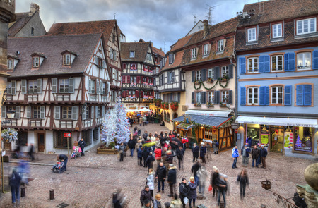 Colmar, France- Decmebr 06,2013: People walking in a town square between traditional half-timber houses and specific Christmas decoration in Colmar, Alsace, France. HDR image with selective motion blur on some of the people. Colmar is considered to be theのeditorial素材