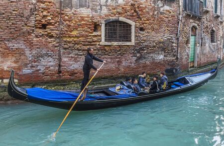 Venice, Italy- February 18th, 2012: A gondola with tourists on a small canal between traditional buildings in Venice, Italy.のeditorial素材
