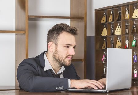 A receptionist working on the laptop at his desk in a small hostel.