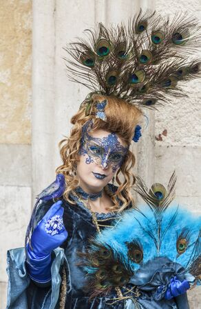Venice,Italy- March 2, 2014: A woman disguised in blue costume with peacock feathers posing in San Marco Square during the Venice Carnival days.のeditorial素材