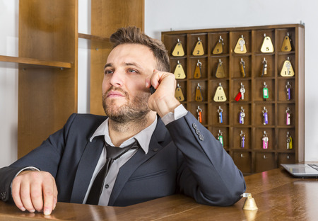 Portrait of a serious receptionist on the phone at his desk in a small hostel.の写真素材