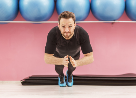 Image of a young handsome man clapping his hands while he is doing pushups in a gym.