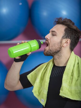 Portrait of a young fit man drinking from a plastic bottle in a gymの写真素材