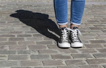 Chartres, France - Spetember 2, 2019: Image of  the lower part of teenager's legs in jeans and All Star Converse sneakers in a cobblestone street.のeditorial素材