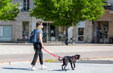 Chartres, France - Avril 18, 2020: Unidentified woman with a protective mask is walking with her dog according to the rules, during the lockdown time due to coronavirus crisis in 2020.のeditorial素材