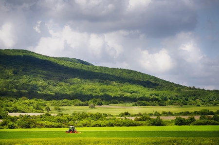 Working Tractor at Agricultural Village Field Around Mountainsの写真素材